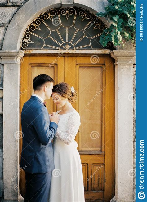 Groom Kisses The Bride On The Forehead Near An Arched Wooden Door Stock