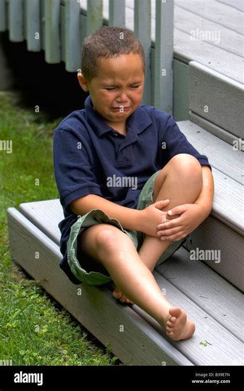 Young Latino Boy Outside Sitting On A Step Holding His Leg In Pain