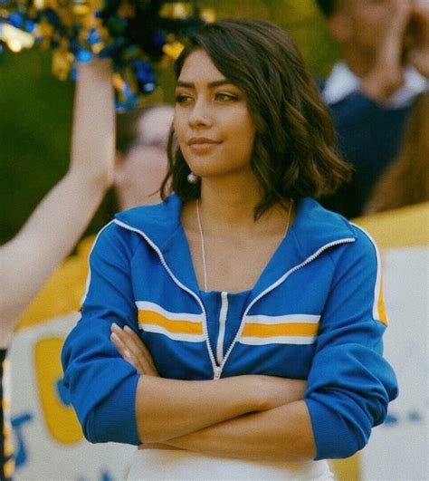 a woman with her arms crossed standing in front of a crowd wearing a cheerleader outfit