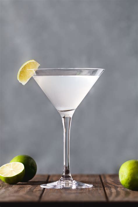 a martini glass with a lemon wedge on the rim and limes next to it