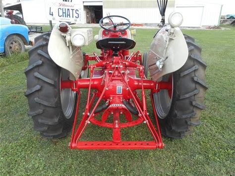 An Old Red And White Tractor Sitting In The Grass With Two Large Tires