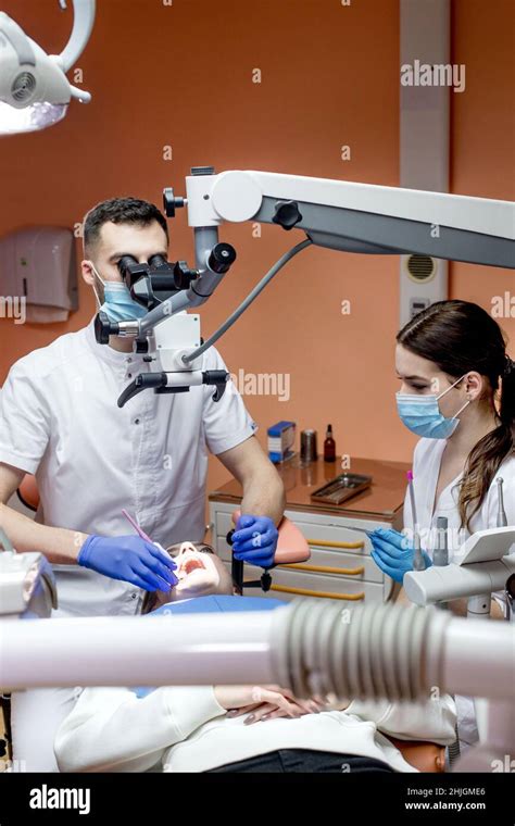 Dentist With Assistant Under Microscope Treats The Patients Teeth