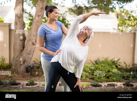 Smiling Trainer Instructing Senior Woman While Exercising At Park Stock