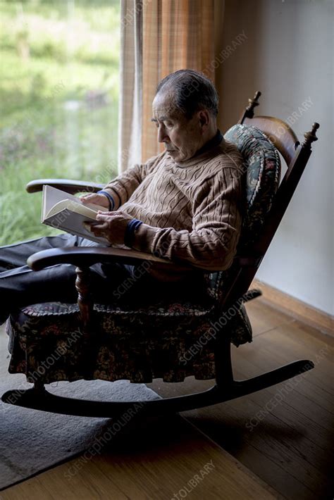 Man Sitting In Rocking Chair By A Window Reading Book Stock Image