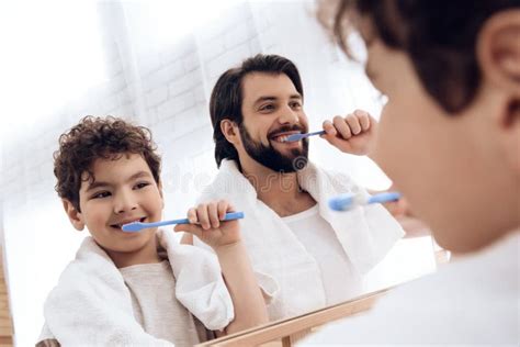 Happy Father And Son Brush Teeth With Toothbrush Looking In Mirror