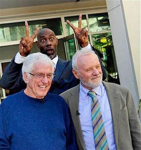 Three Men Standing In Front Of A Building Posing For The Camera With Their Fingers Up