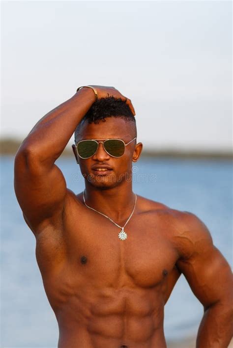 muskulöser junger athletischer sexy mann auf dem strand mit einem nackten torso in der