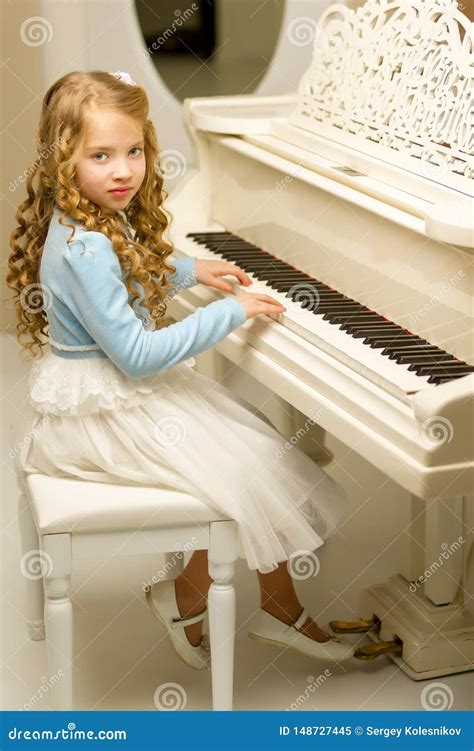 Beautiful Little Girl Is Playing On A White Grand Piano Royalty Free