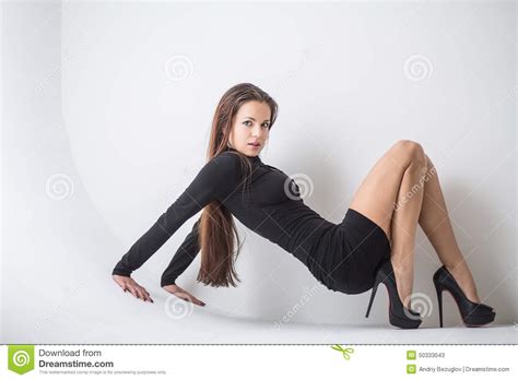 Aantrekkelijk Brunette In Een Korte Zwarte Kleding Die Op De Vloer Zitten Stock Afbeelding