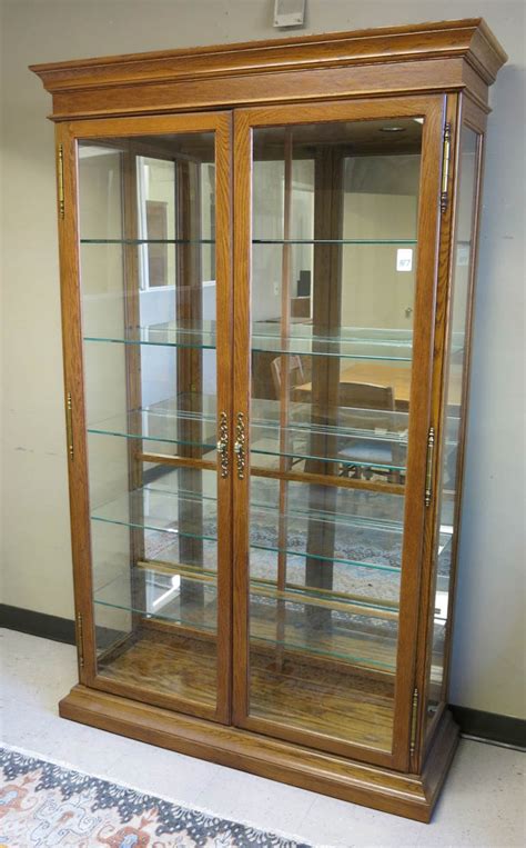 It features a solid wood frame in a square shape with a glass top, incorporated with a metal latch lock that keeps your items safe and secure. MODERN OAK AND GLASS ILLUMINATED DISPLAY CABINET,