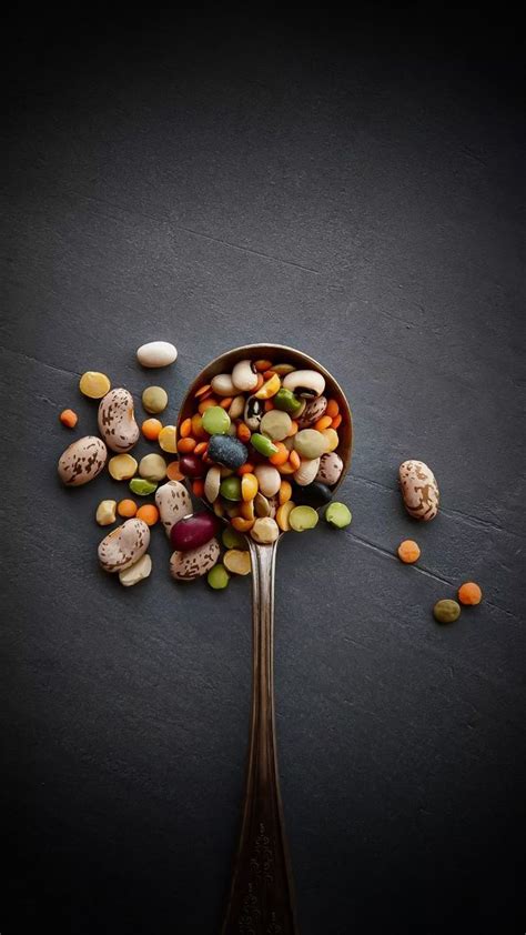 A Spoon Filled With Lots Of Different Types Of Beans On Top Of A Black