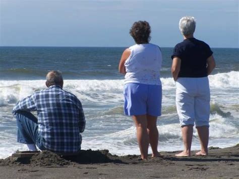 Three People Are Sitting On The Beach Watching The Waves Come In To