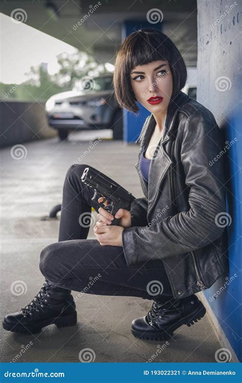beautiful brunette spy agent killer or police woman in leather jacket and jeans with a gun in