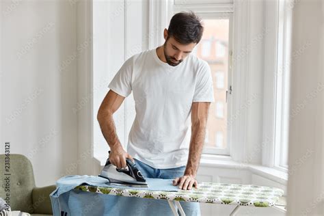 Hard Working Bearded Man Dressed In White T Shirt Irons Shirt On