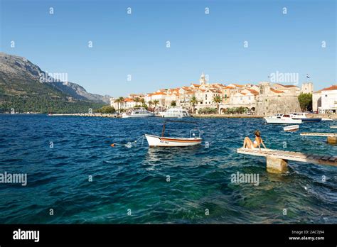 woman in bikini on jetty sunbathes in front of the panorama of the old town of korčula in the