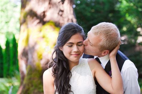 caucasian groom lovingly kissing his biracial bride on cheek di stock image image of love
