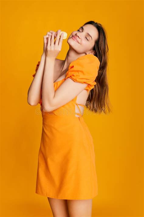 portrait of beautiful brunette girl in cute dress posing over orange background sweet dessert