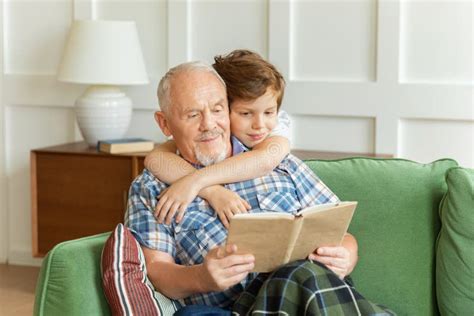 Grandson Embracing Grandpa Sitting On Couch Reading Book Stock Image