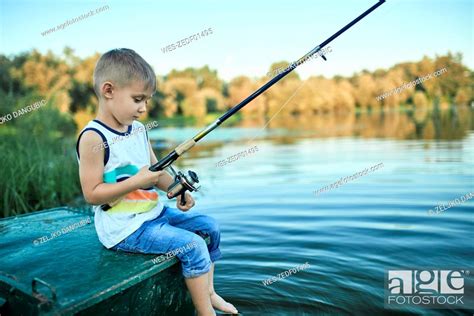 Back View Of Little Boy With Fishing Rod Sitting On Boat Stock Photo