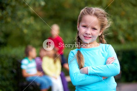 Portrait Of Happy Girl Crossing Arms And Looking At Camera With Her Friends On Background