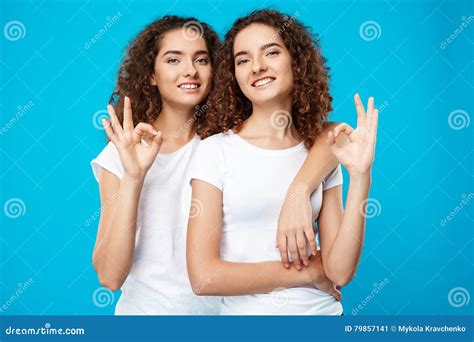 Two Pretty Girls Twins Smiling Showing Okay Over Blue Background Stock Image Image Of