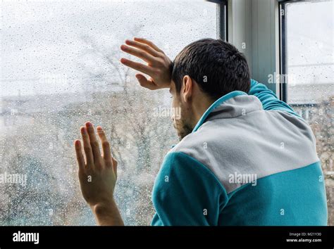 Depressed Young Man Upset With Bad News Looking Through Rainy Window