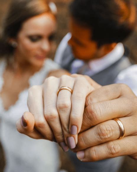 A Bride And Groom Holding Hands In Front Of Each Other With Their Wedding Rings On Their Fingers
