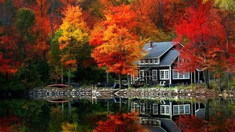 A House Sitting On Top Of A Lake Surrounded By Colorful Trees In The