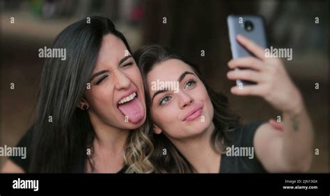 Girlfriends Taking Selfie Sticking Tongue Out Young Women Posing For Photo Holding Smartphone