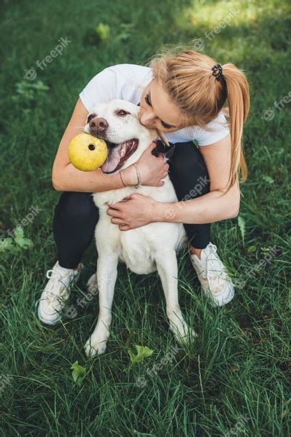 Blonde Caucasian Woman Embrasse Son Chien Tout En Jouant Dans Un Parc Verdoyant Avec Un Ballon