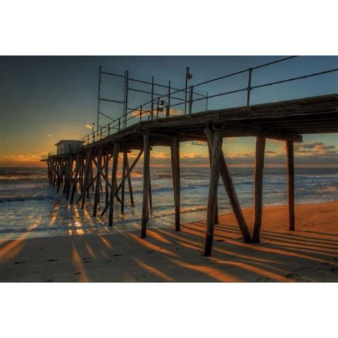 The Sun Is Setting At The End Of A Long Pier On The Beach With Waves