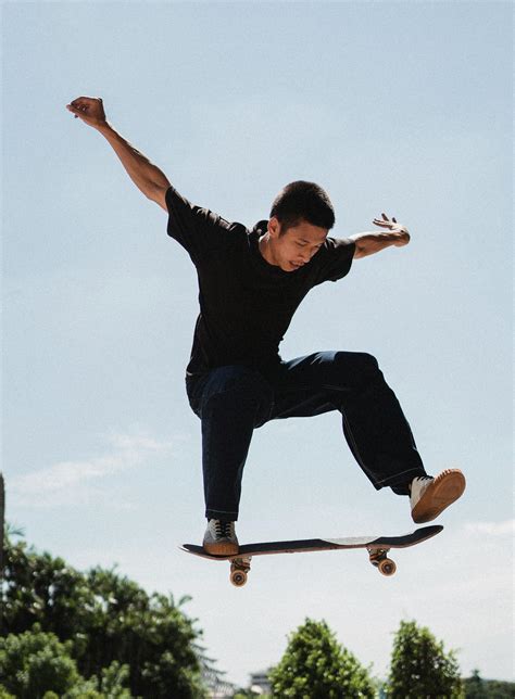 Confident Young Man Performing High Jump On Skateboard On Sunny Day