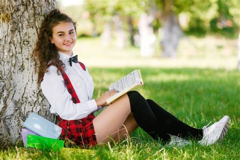 Schönes Schulmädchen In Einer Karierten Roten Schuluniform Sitzt In Einem Park Nahe Einem Baum