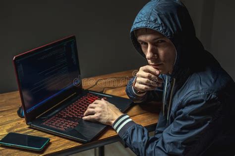 Hacker In A Hood With A Phone Is Typing On A Laptop Keyboard In A Dark