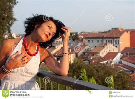 portrait of a lady on a balcony looking at the city wearing a white dress red necklace wavy