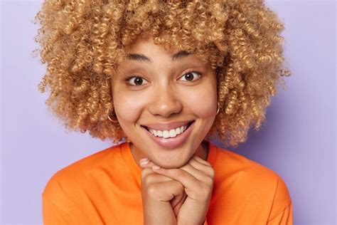 Premium Photo Close Up Portrait Of Cheerful Woman With Curly Hair Keeps Hands Under Chin