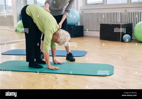 Senior Woman Bending Forward And Touching Her Toes Being Helped By Gym