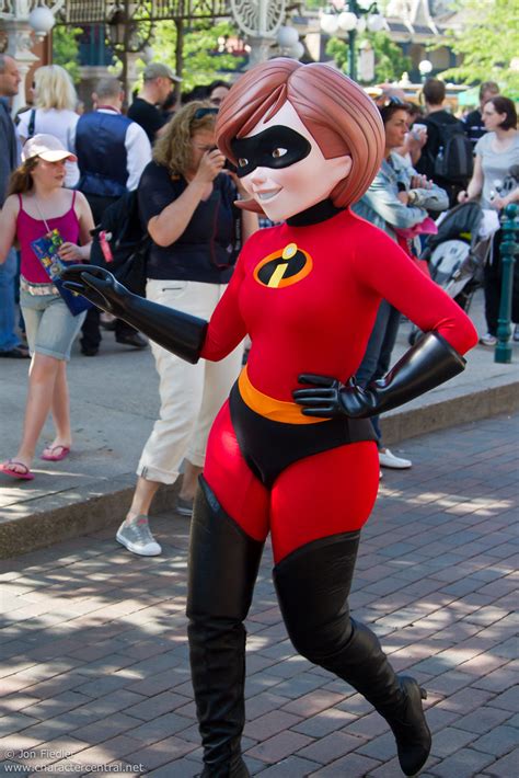 A Woman In A Red And Black Costume Is Running Down The Street While