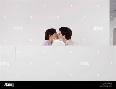 Side View Of A Business Couple Kissing In Office Cubicle Stock Photo