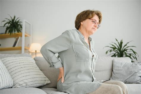 Mujer madura sentada en la cama y tocándose la espalda con radiculitis