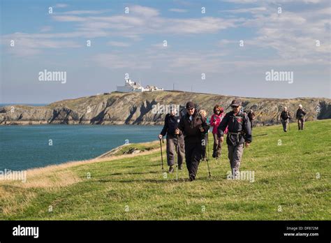 Ramblers Group Of Walkers Walking On Coastal Path With Point Lynas