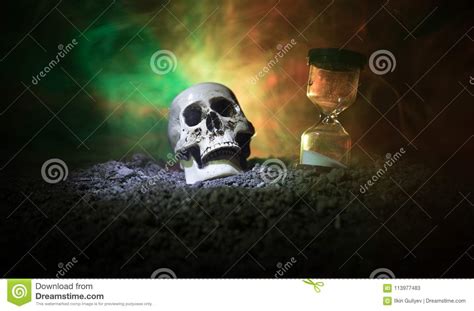 Skull And Vintage Hourglass On Dark Toned Foggy Background Under Beam Of Light Horror Concept