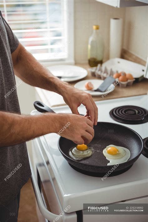 Mid Section Of Man Cracking An Egg Into A Frying Pan In The Kitchen At