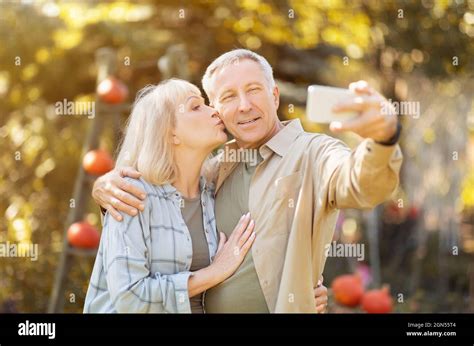 senior couple spending time in sunny garden together taking selfies woman kissing husband in