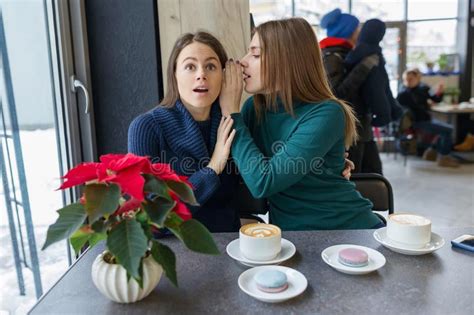 Two Young Beautiful Women Secretly Sitting At A Table In A Coffee Shop