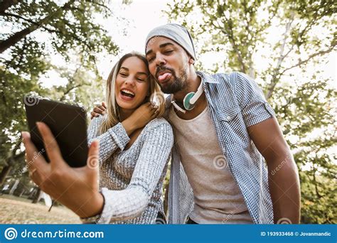 Romantic And Happy Mixed Race Young Couple In Park Using Digital Tablet