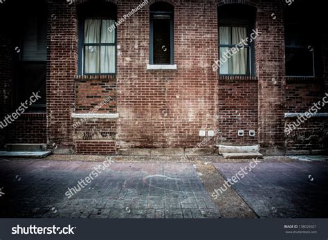 A Brick Alleyway With Concrete Walkway Old Windows And Doors Made Of