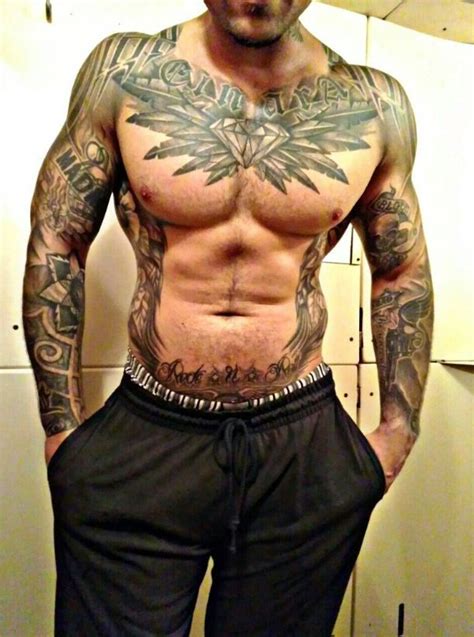 A Man With Tattoos On His Chest Standing In Front Of A Mirror