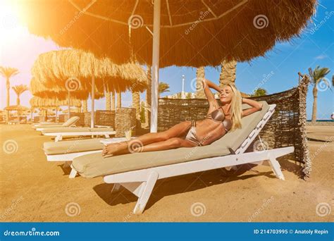 Woman Wearing Bikini Sitting On Lounger Under Straw Canopy Umbrella At
