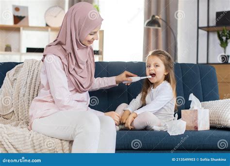 Young Smiling Muslim Mother In Hijab And Her Daughter Sitting At Home